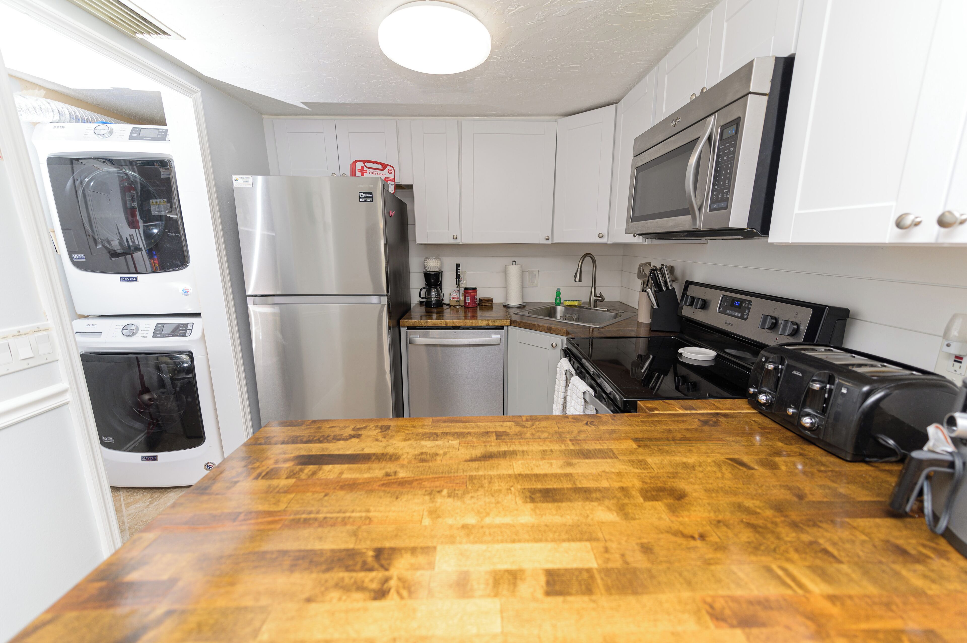 A compact kitchen with white cabinets, a stainless steel refrigerator, a microwave, a toaster, and a dishwasher.