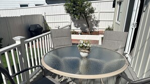 A round glass table with four chairs, a potted plant, and a white fence in the background.