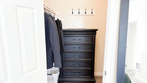 A hallway with a dark wooden dresser, a coat rack with clothes, and a laundry basket.