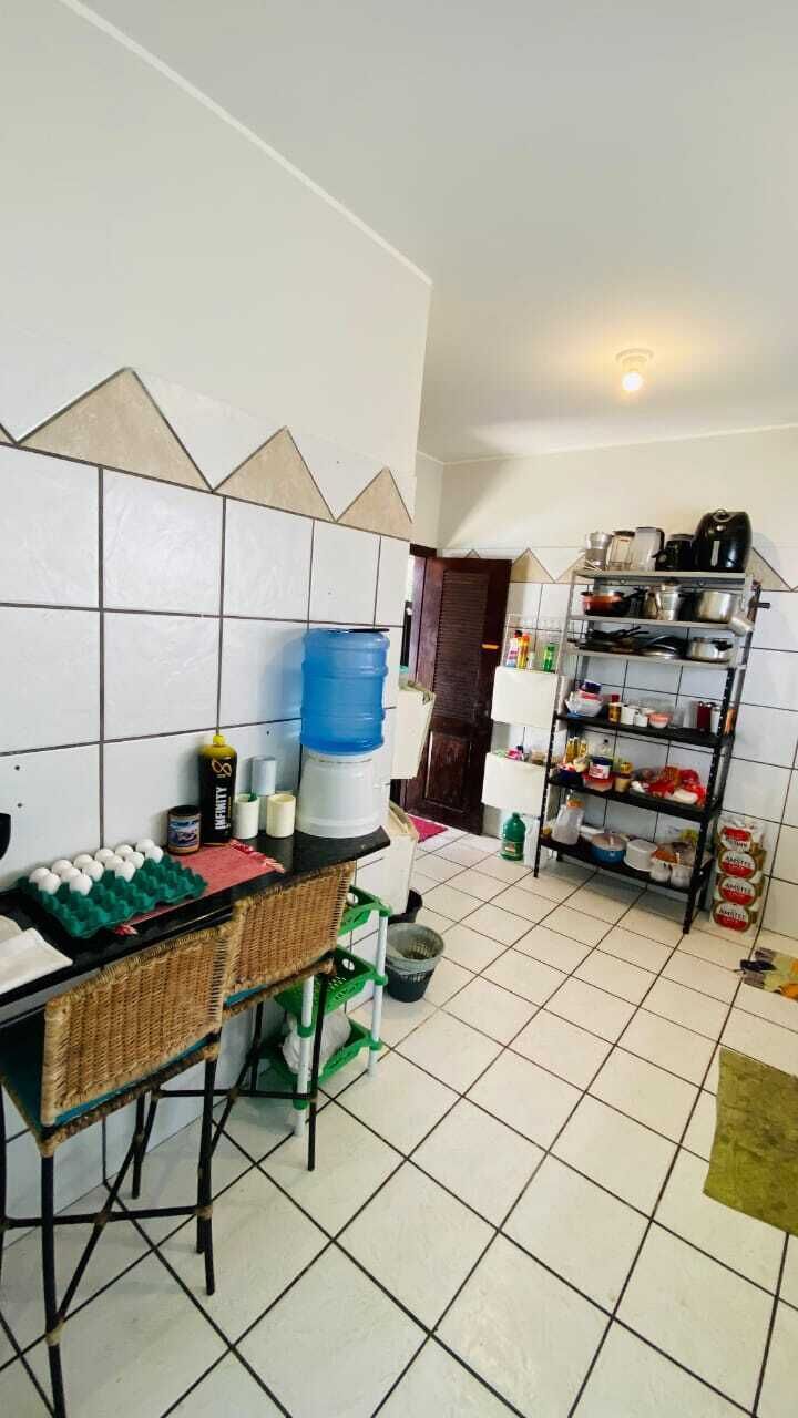Une cuisine avec un crédence carrelée, un distributeur d’eau, une étagère contenant des ustensiles de cuisine et un coin repas avec une table et des chaises.
