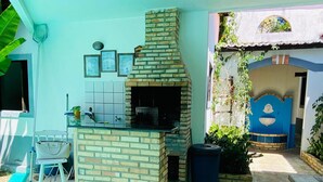 Un patio exterior con zona de barbacoa de ladrillo, una pequeña mesa con una silla y una pared azul con un adorno.