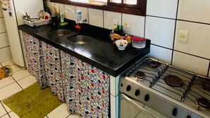 Una cocina con encimera negra, estufa y ventana sobre el lavamanos.