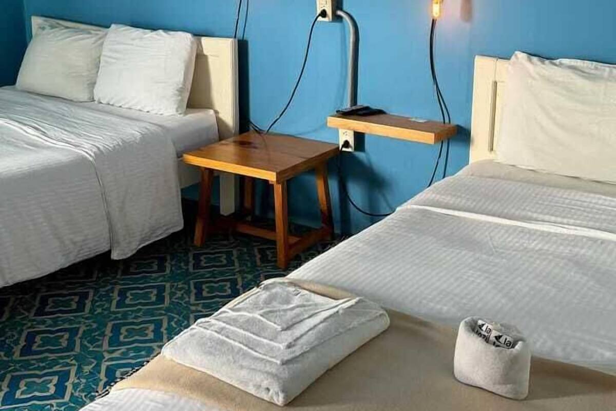 Hotellihuone, jossa on kaksi sänkyä, puinen yöpöytä ja kuviollinen lattia.