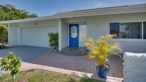 A single-story house with a blue front door, a garage, and a small front yard with potted plants. - Tropical Getaway! Gulf access with heated pool! (Cape Coral)