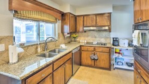 A kitchen with wooden cabinets, granite countertops, a stainless steel sink, and a microwave. - Tropical Getaway! Gulf access with heated pool! (Cape Coral)