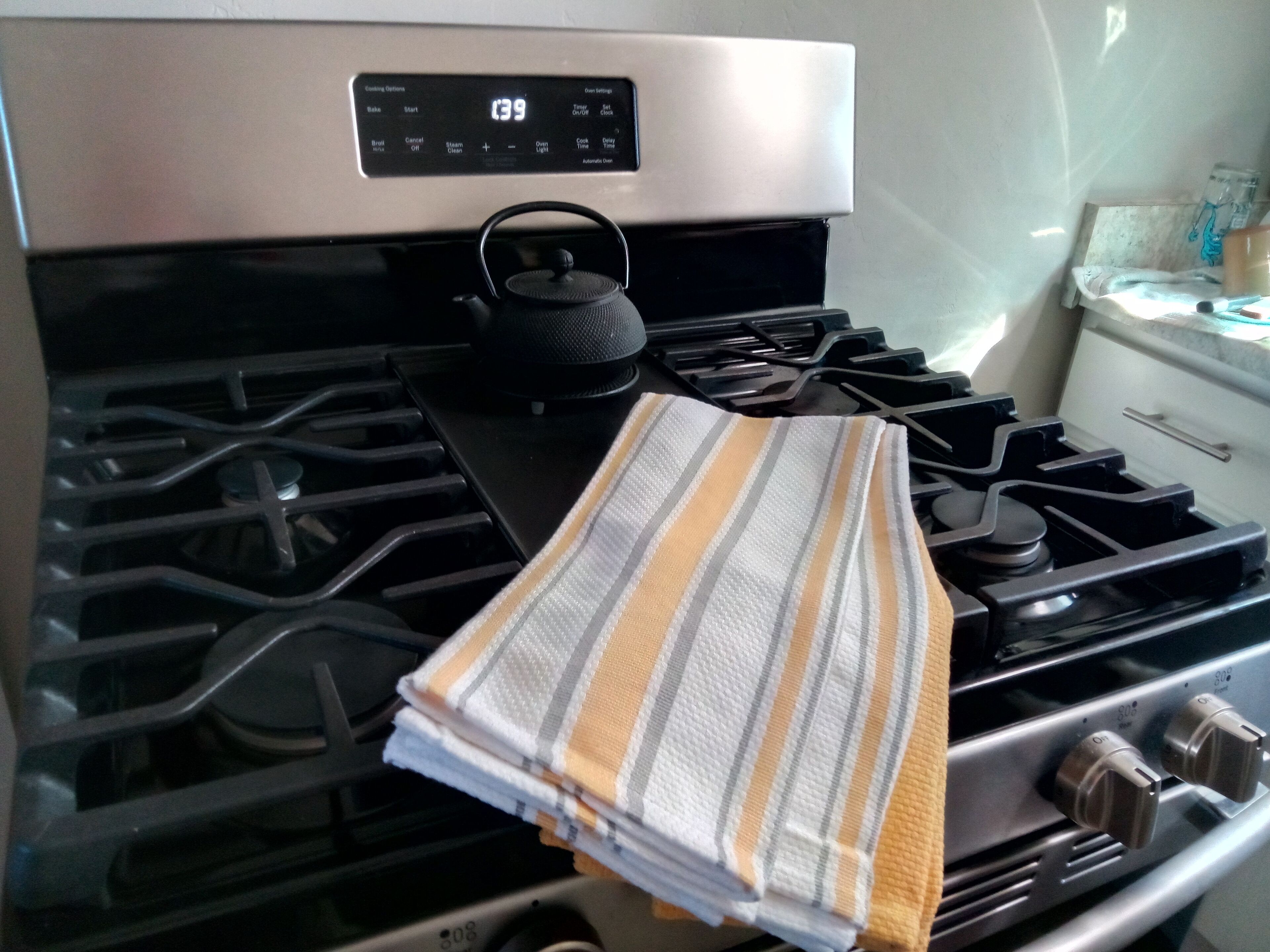 A kitchen with a stainless steel range hood, a kettle, and a striped towel on the stove.