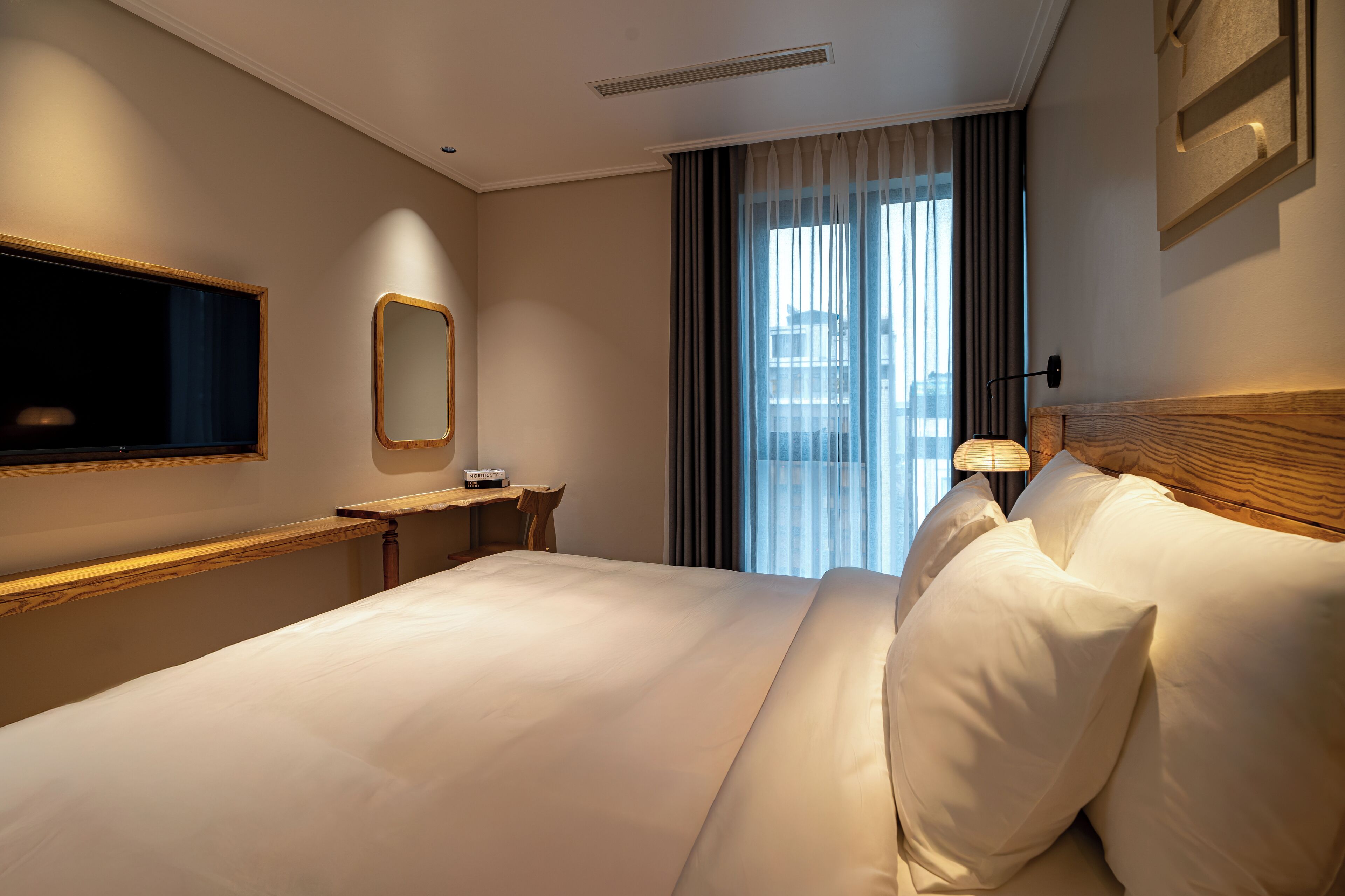 A hotel room with a large bed, a desk, a TV, and a window with curtains.