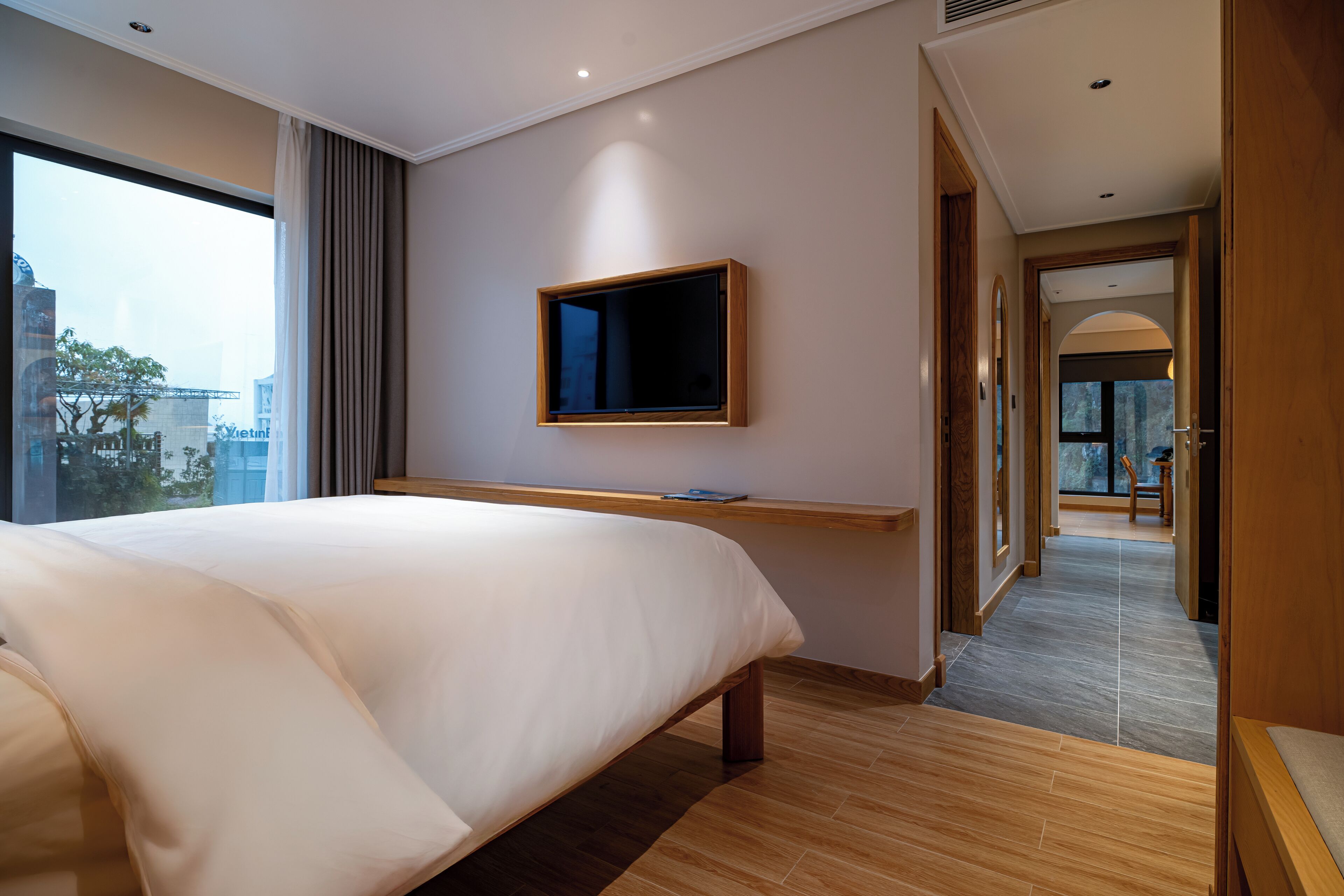 Une chambre d’hôtel moderne avec un grand lit, un téléviseur à écran plat fixé au mur et une vue sur la ville par la fenêtre.