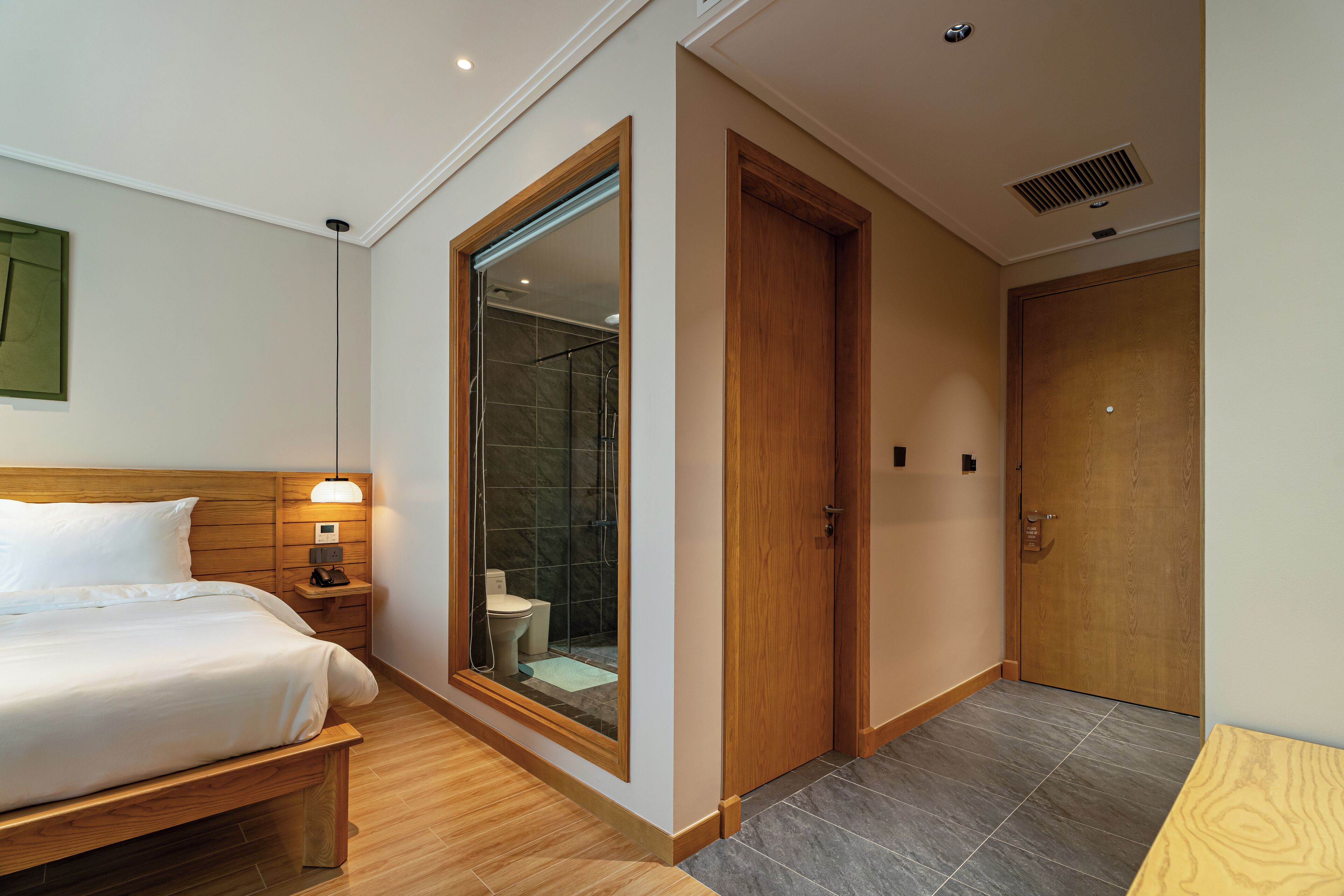 Une chambre d’hôtel comprenant un lit, une table de chevet, un grand miroir, une porte en bois et un espace douche.
