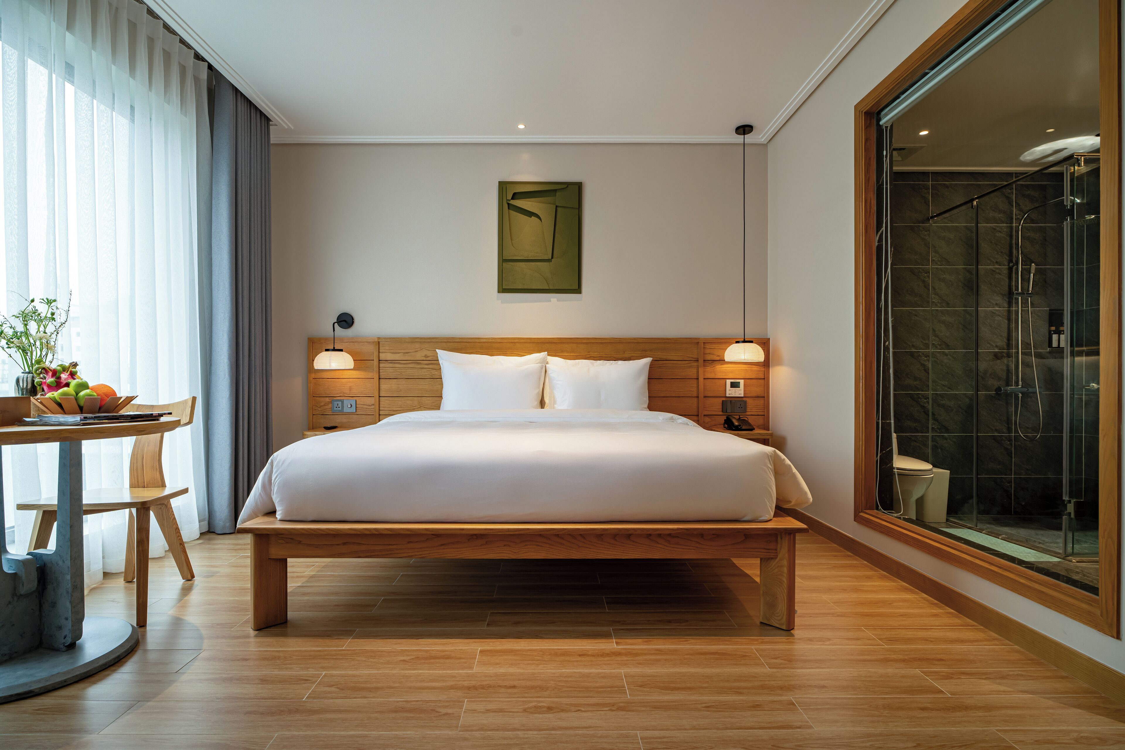 Um quarto espaçoso com uma cama grande, mesas de cabeceira, um painel de cabeceira de madeira, uma obra de arte na parede e um box de vidro.