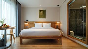 Ein geräumiges Schlafzimmer mit einem großen Bett, Nachttischen, einem hölzernen Kopfteil, einem an der Wand befestigten Kunstwerk und einer Duschkabine aus Glas.