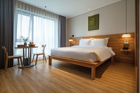 A hotel room with a large bed, wooden headboard, bedside tables, a small table with chairs, and a large window with curtains. - Nam Dat Hotel by D'Lecia Ha Long (Ha Long)