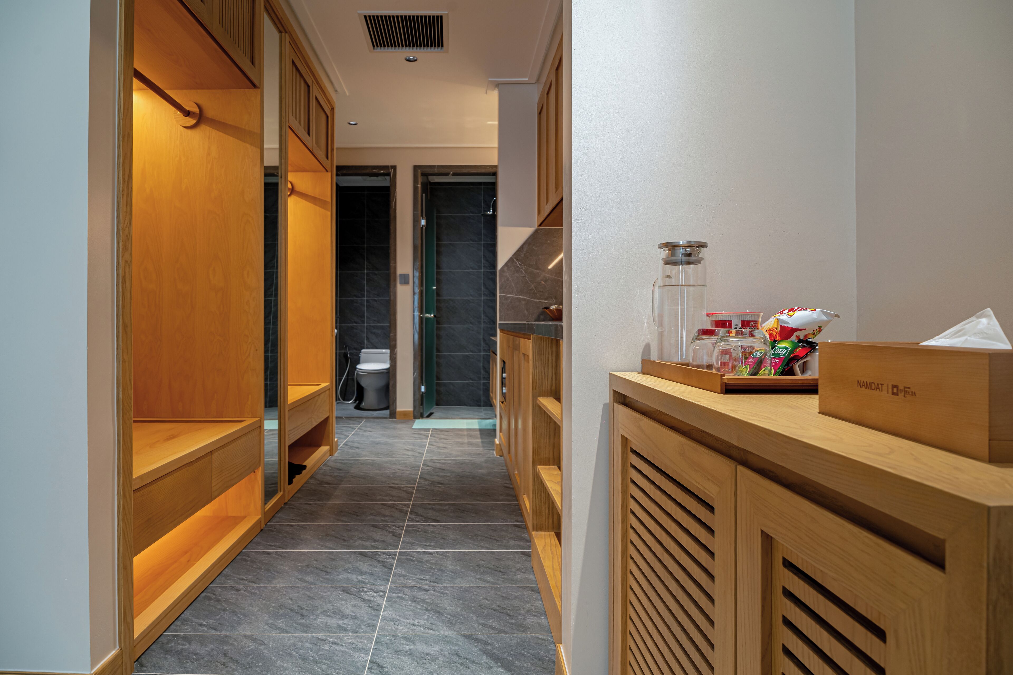 A hotel corridor with wooden shelving, a reception desk, and a tiled floor.