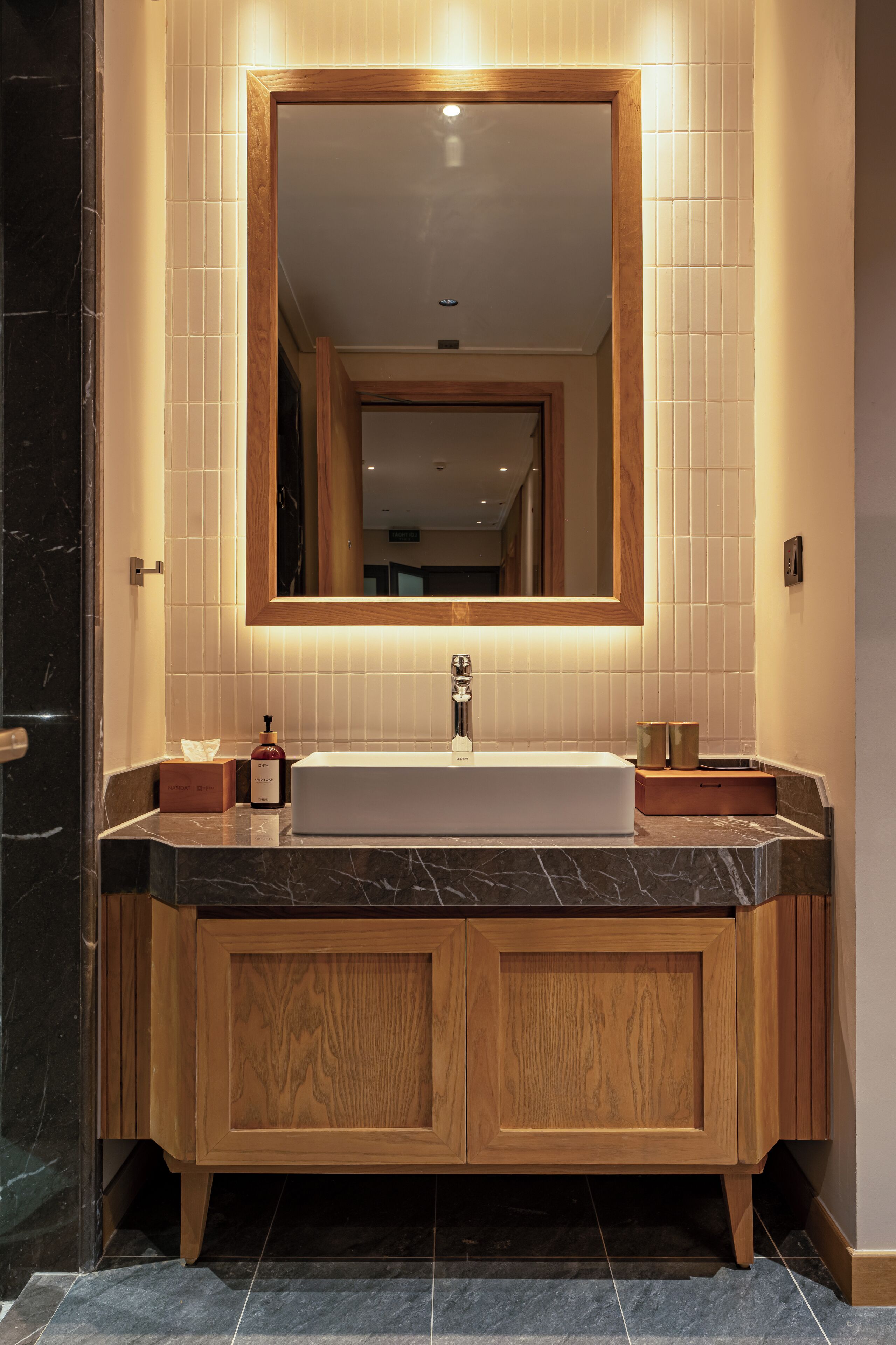 Un baño moderno con un espejo grande, tocador de madera y lavamanos blanco.
