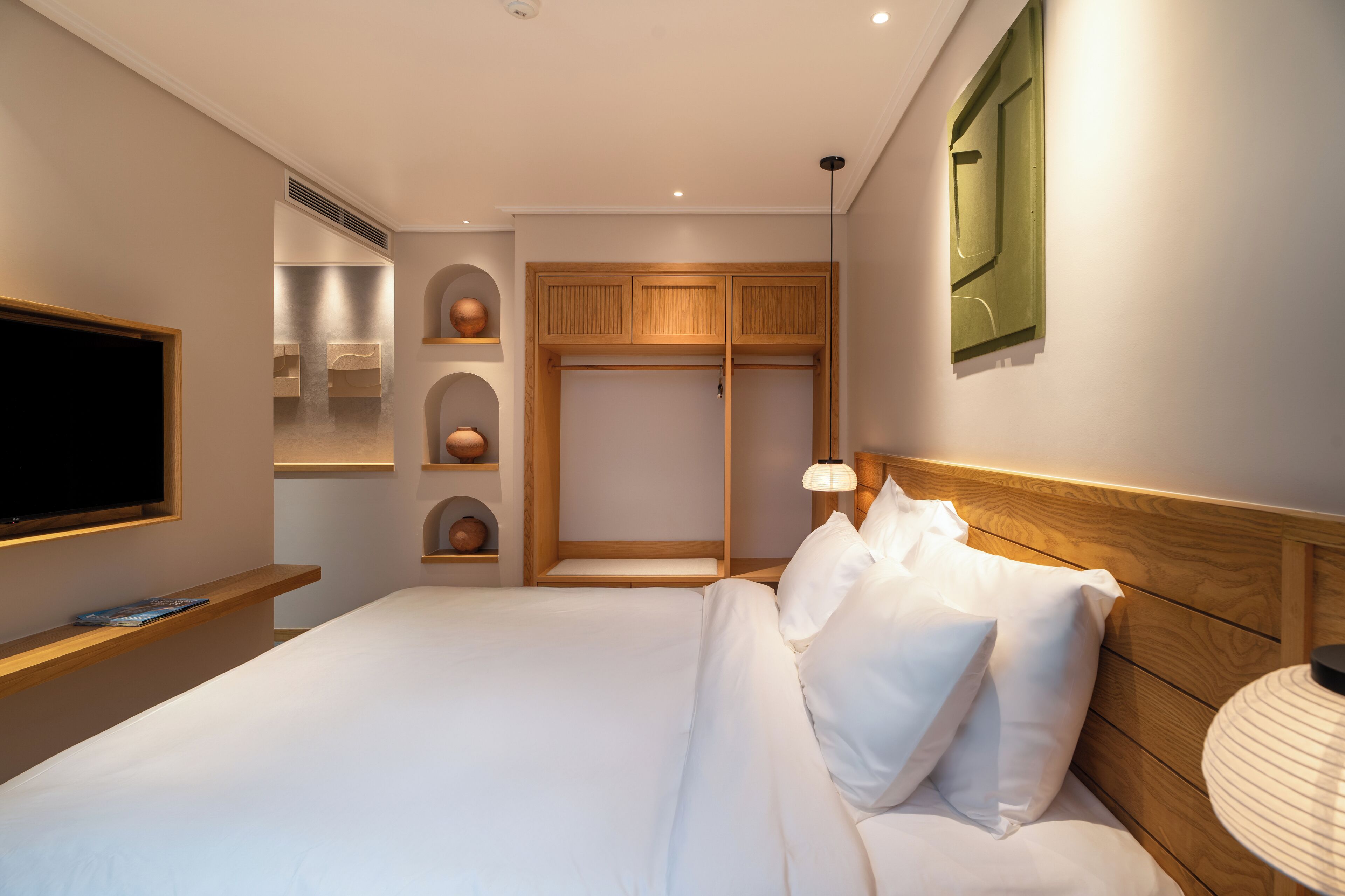 A modern hotel room with a large bed, built-in wardrobe, and a flat-screen TV.