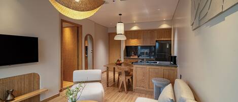 Una sala moderna con sofá, una mesa de centro y televisor. Hay una zona de cocina con armarios de madera y una mesa de comedor.