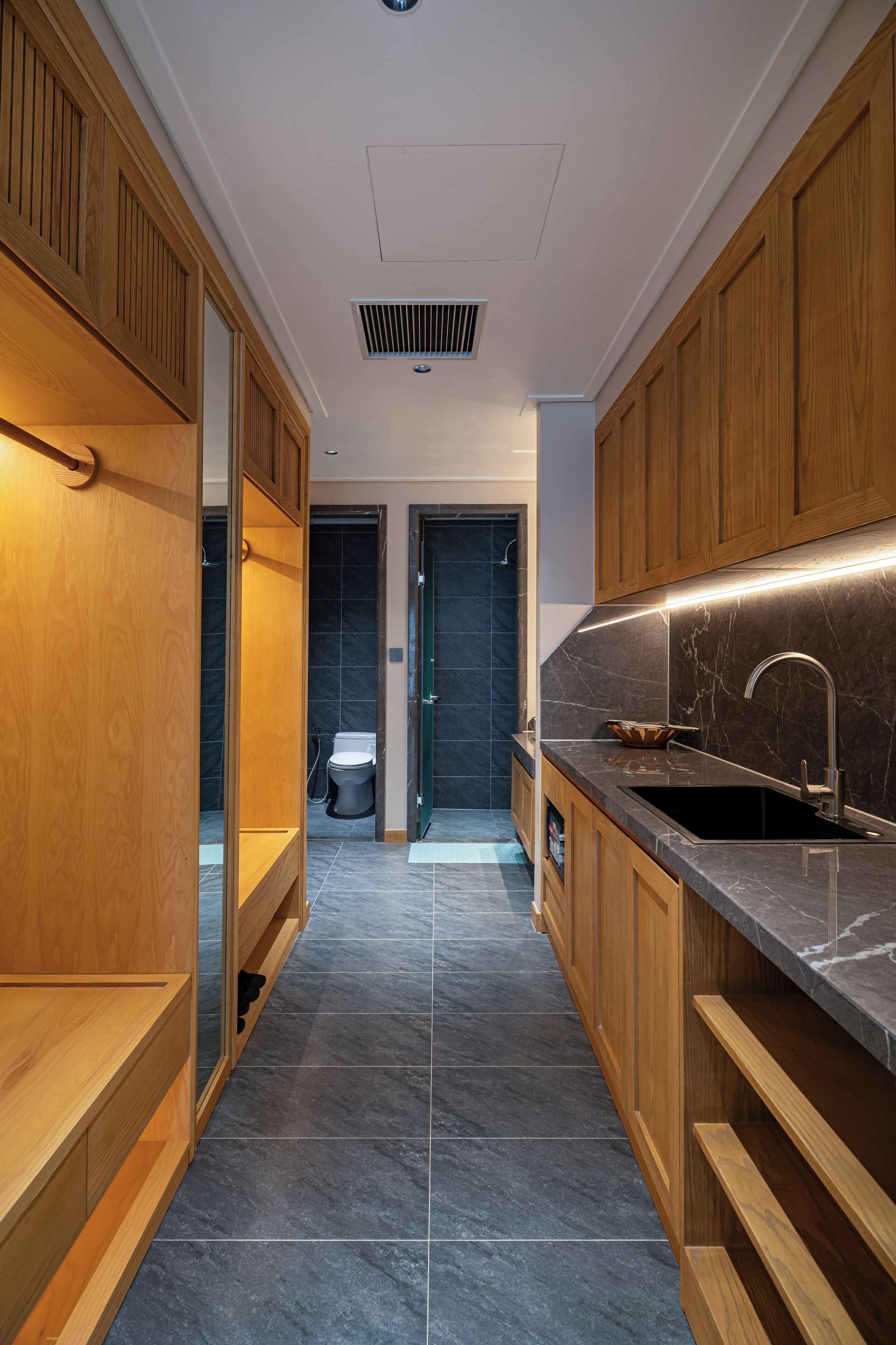 A modern kitchen with wooden cabinets, a black countertop, and a stainless steel sink.