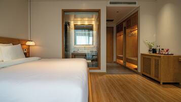 Una habitación de hotel moderna con una cama grande, un armario de madera, un tocador con espejo y un mueble pequeño con artículos de aseo.