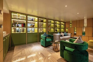 A modern interior with green and wooden accents, featuring a seating area with green upholstered chairs and a white sofa, and a bar area with glass display shelves. - Nam Dat Hotel by D'Lecia Ha Long (Ha Long)
