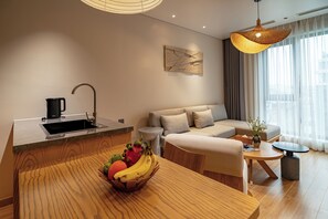 A modern living room with a wooden dining table, a sofa, a coffee maker, and a fruit bowl. - Nam Dat Hotel by D'Lecia Ha Long (Ha Long)