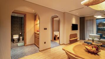 A modern hotel room with a wooden dining table, a TV mounted on the wall, and a view of the outdoors through the window.