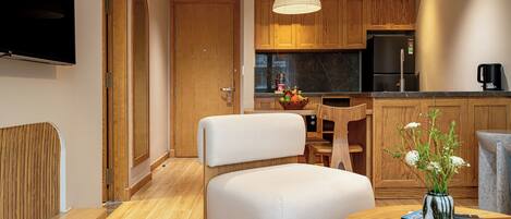 A modern kitchen with wooden cabinets, a built-in refrigerator, and a dining area with a white chair and a table.