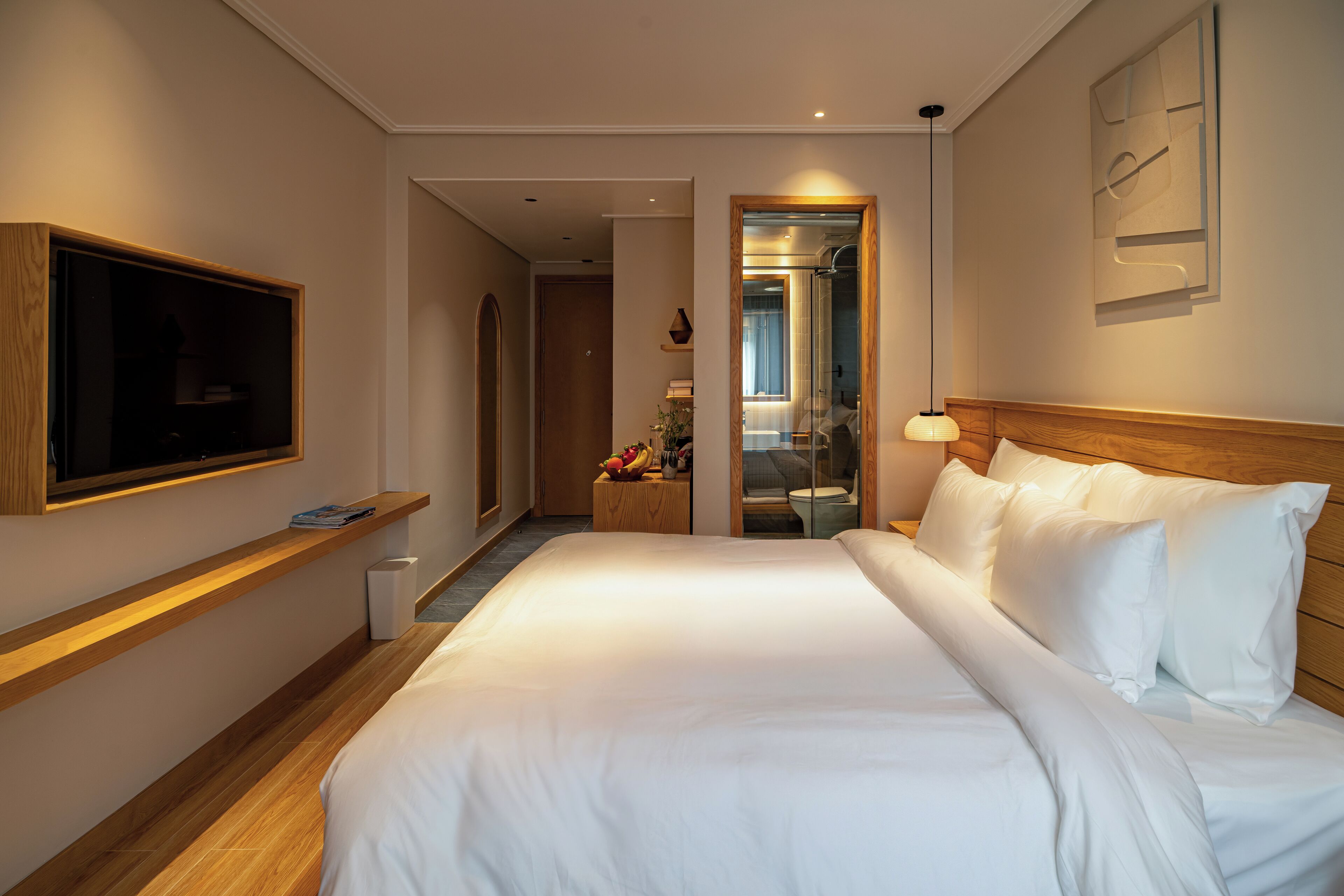 Hotelkamer met een groot bed, een aan de muur bevestigde televisie, een houten hoofdbord en een klein nachtkastje met een lamp.