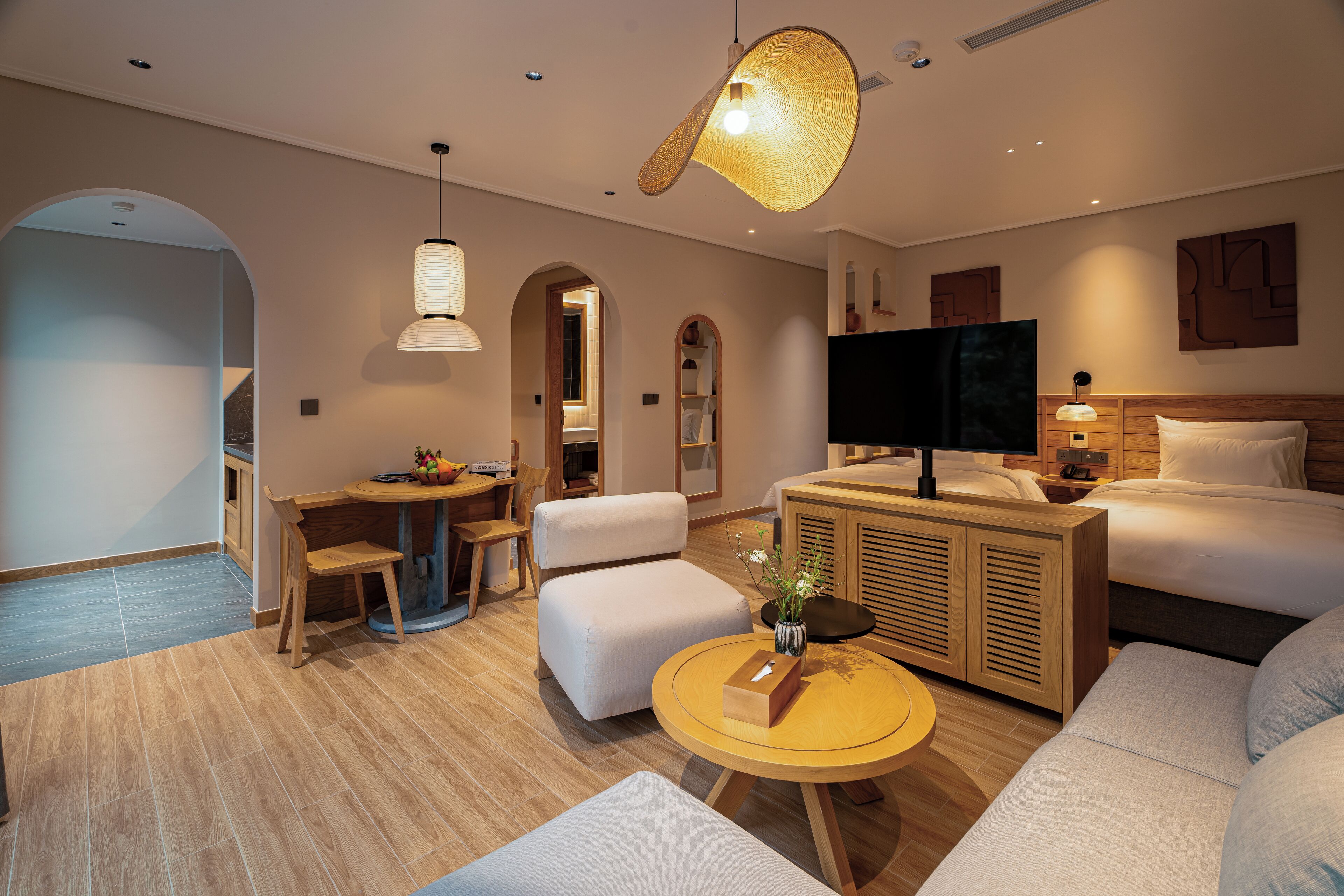 A modern hotel room with a sofa, a round coffee table, a TV, and a wooden cabinet.