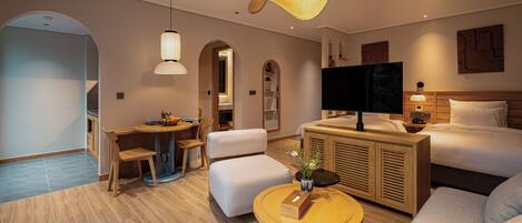A modern hotel room with a sofa, a round coffee table, a TV, and a wooden cabinet.
