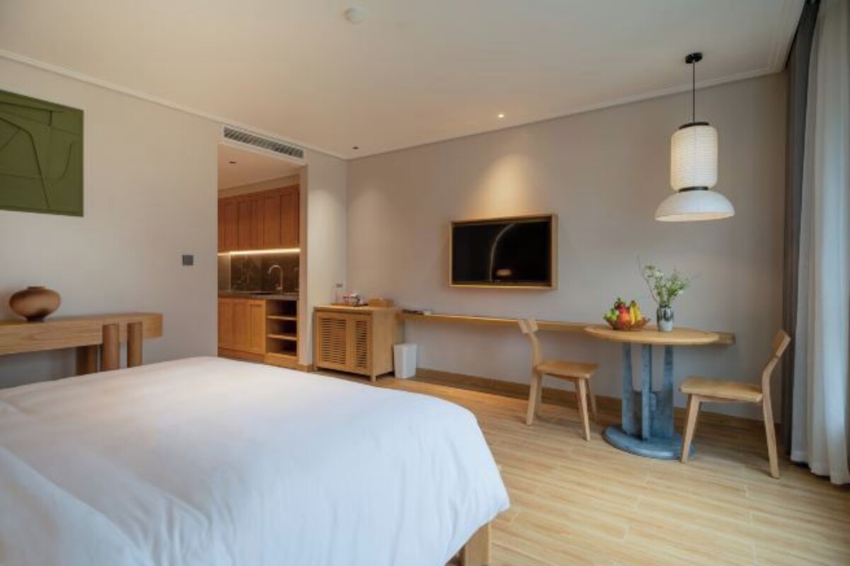 Una habitación de hotel moderna con una cama grande, un área de comedor con una mesa y sillas, una kitchenette y un televisor montado en la pared.