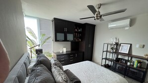A bedroom with a bed, a ceiling fan, a wardrobe, a shelf with decorative items, and a window with blinds.