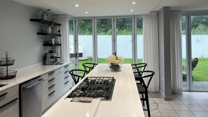 A modern kitchen with a central island, built-in appliances, and a view of a green garden through large sliding doors.