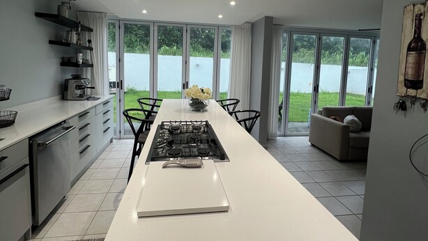 A modern kitchen with a central island, large windows, and a view of greenery.