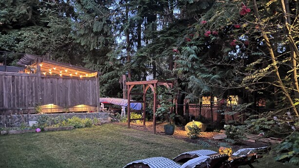 Ein Garten mit einer Holzterrasse, einer Pergola und einer Sitzgruppe mit Liegestühlen.