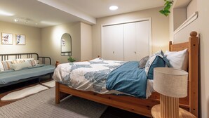 Ein Schlafzimmer mit einem hölzernen Bett, einem Nachttisch mit Lampe, einem kleinen Schreibtisch, einem Stuhl, einem Kleiderschrank und einem Spiegel.