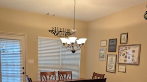 A dining room with a wooden table and chairs, a chandelier, and framed pictures on the wall. - Masters Rental - Walking Distance + WFH Spaces! (Augusta)