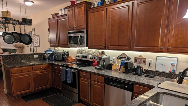 A kitchen with wooden cabinets, granite countertops, stainless steel appliances, and a black floor mat. - Masters Rental - Walking Distance + WFH Spaces! (Augusta)