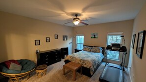 A bedroom with a bed, a treadmill, a chair, a dresser, and a ceiling fan. - Masters Rental - Walking Distance + WFH Spaces! (Augusta)