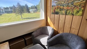 Ein Zimmer mit großem Fenster, einem Landschaftsbild und zwei grau gepolsterten Sesseln.
