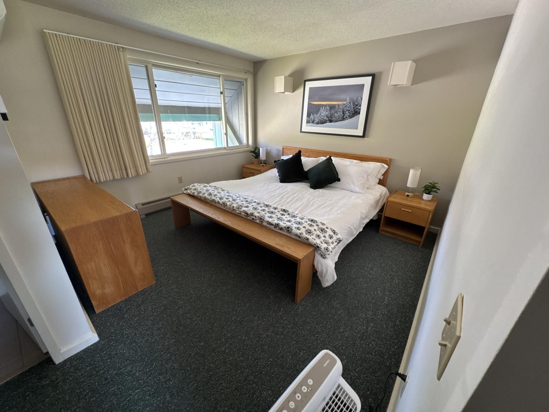 A bedroom with a bed, bedside tables, a bench, a window with curtains, and a framed picture on the wall.