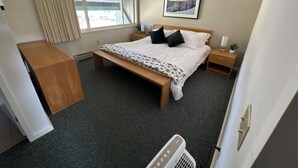 Ein Schlafzimmer mit einem Bett, Nachttischen, einer Bank, einem Fenster mit Vorhängen und einem gerahmten Bild an der Wand.