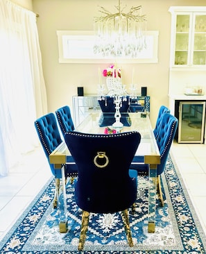 A dining room with a glass table, blue upholstered chairs, a chandelier, and a patterned rug. - Spacious 4-Bedroom Retreat next to Welland Waterpark – Perfect for Families!"
(Welland)