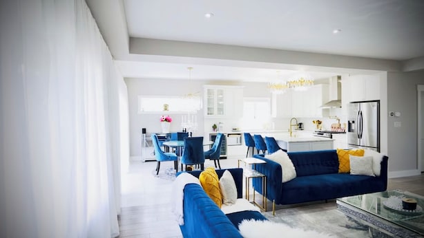Ein modernes Wohnzimmer mit einem blauen Sofa, einem Glastisch und einem Essbereich mit blauen Stühlen.
