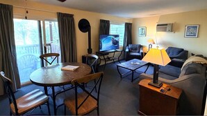 Een woonkamer met een televisie, een bank, een salontafel, een lamp en een eethoek met stoelen en een tafel.