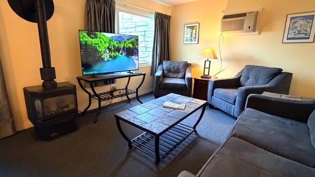 Een woonkamer met een televisie, een bank, een fauteuil, een tafel, een lamp en een open haard.