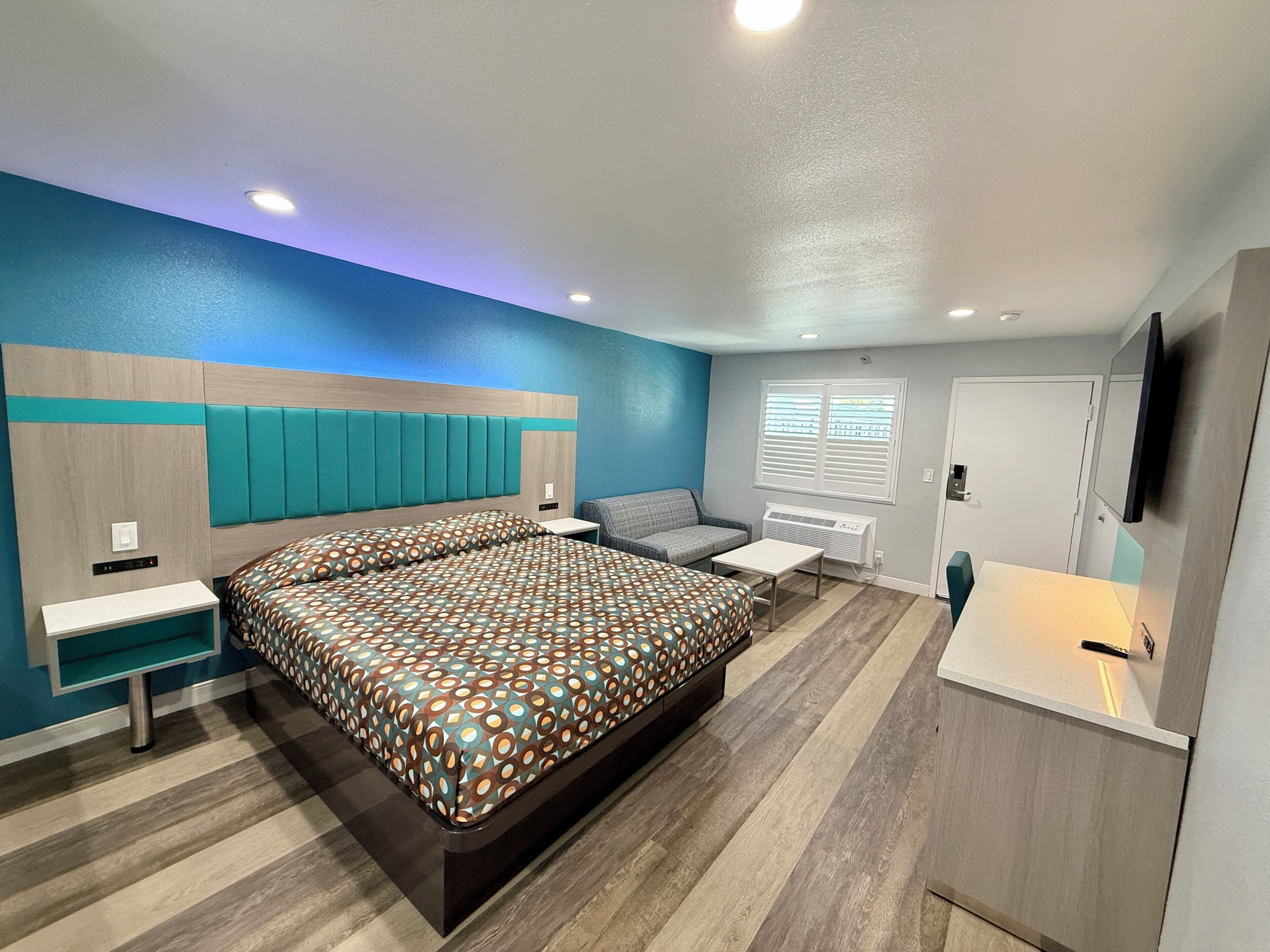 Quarto moderno com uma cama grande, mesa de cabeceira, uma cadeira, escrivaninha e televisão.