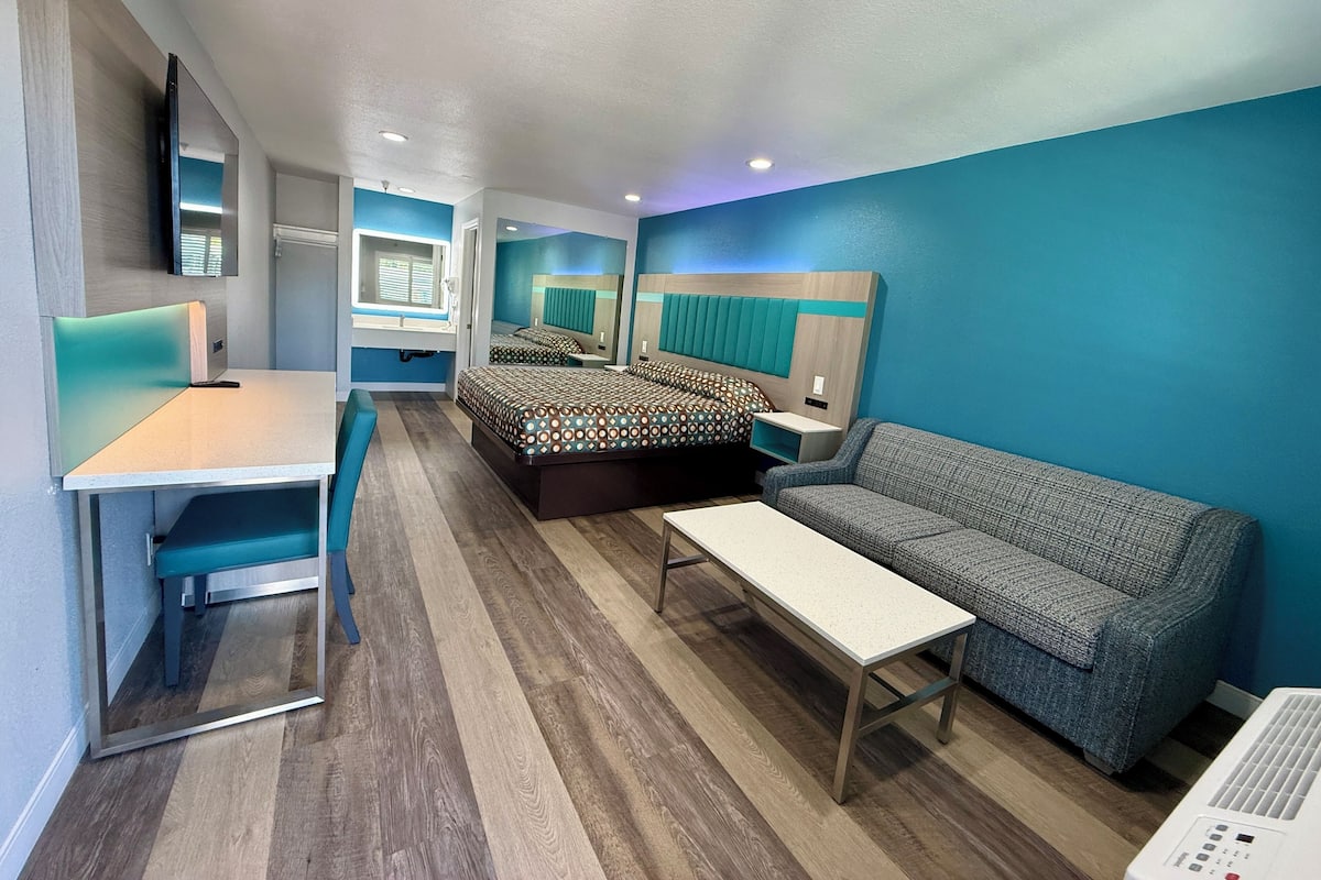 A modern hotel room with a bed, a sofa, a desk, and a mirror.