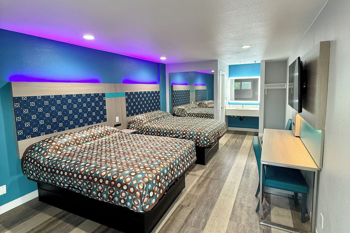 A modern bedroom with two beds, a desk, and a TV.