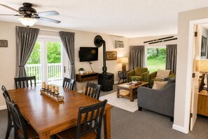 A cozy living room with a wooden dining table, chairs, a sofa, a television, and a fireplace. - Charming Stay in Stowe Condo: Hot Tub&Indoor Pool (Stowe)