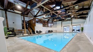 An indoor swimming pool with a concrete floor, wooden beams, and a view of the outside through large windows. - Charming Stay in Stowe Condo: Hot Tub&Indoor Pool (Stowe)